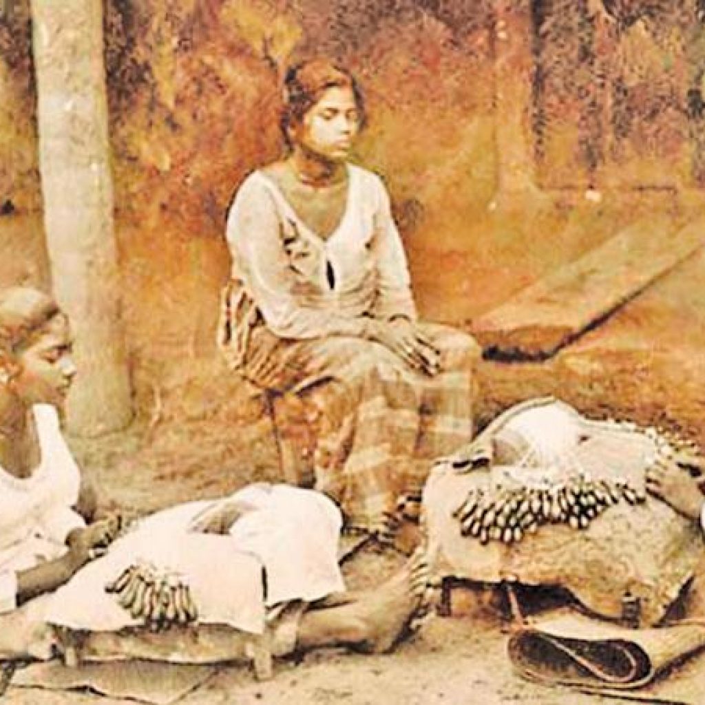 Two women sit near baskets filled with harvested finger millet