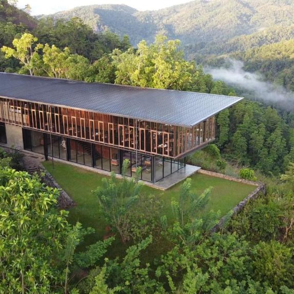 Modern glass villa on hilltop surrounded by lush green forest