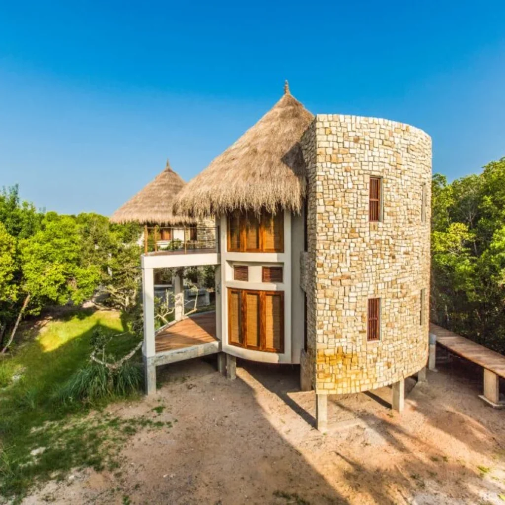 Eco-style round stone villa with thatched roof surrounded by greenery