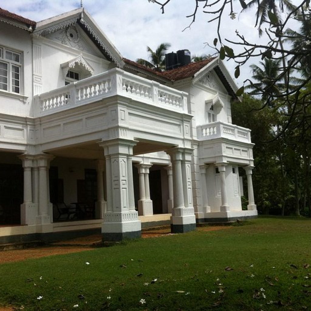 Colonial-era white mansion with ornate pillars and red-tiled roof in tropical setting