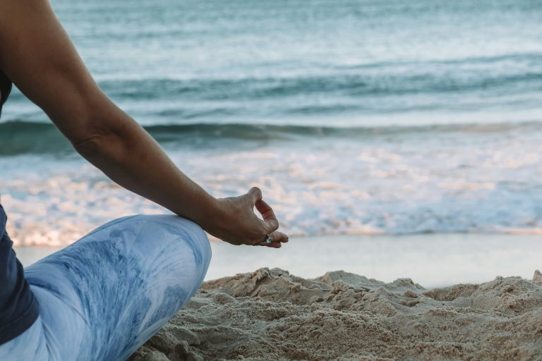 A person meditating in lotus pose on sandy beach with ocean waves in background